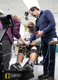  Dr. Ron Triolo (right) and colleague test a device that will stimulate nerves in a Veteran's paralyzed legs to help him operate a rowing machine. (Photo by Cleveland VA Medical Center.)