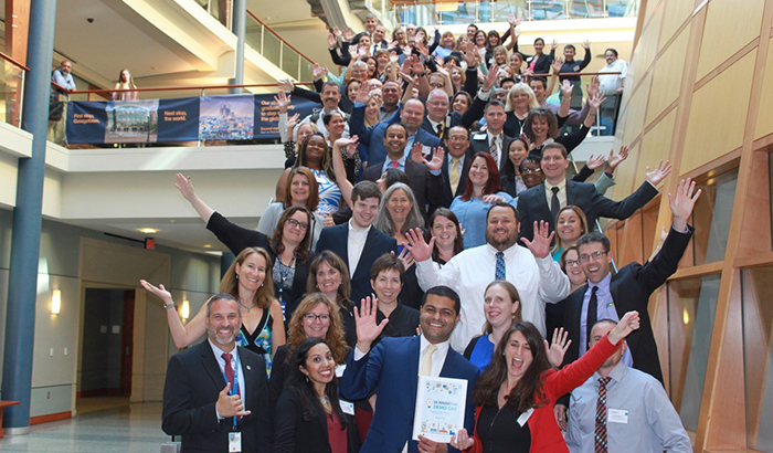 Andrea Ippolito, head of the VA Innovators Network (front center, in red jacket), and VA Assistant Deputy Under Secretary Shereef Alnahal (front center, in blue suit) join attendees of  VA Innovation and Demo Day for a group photo. (VA photo) 