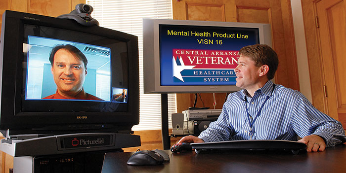 In this 2008 image, Drs. John Fortney (on screen) and Jeffrey Pyne chat through a video system used to bring PTSD therapy to Veterans in rural areas. Since the early days of the research, it has progressed toward larger trials and implementation efforts within VA. (Photo by Jeff Bowen) 