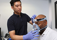 Research technician Michael Tam fits a CPAP mask on Ralph Liggins.  
