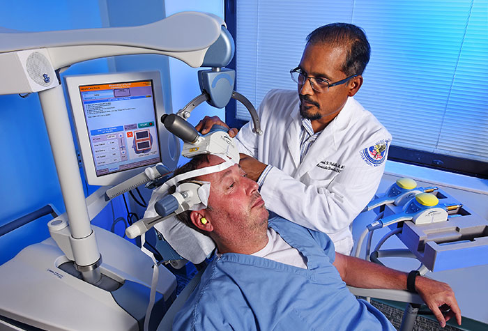 Dr. Prasad Padala demonstrates how repetitive transcranial magnetic stimulation works with the help of a staff member at the Little Rock VA. (Photo by Jeff Bowen)) 