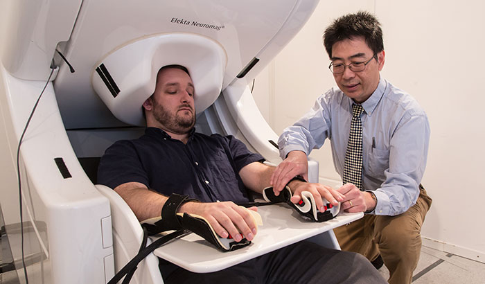 Dr. Mingxiong Huang prepares to do a MEG brain scan on a “healthy control” who has participated in his neuroimaging research. (Photo by Kevin Walsh) )