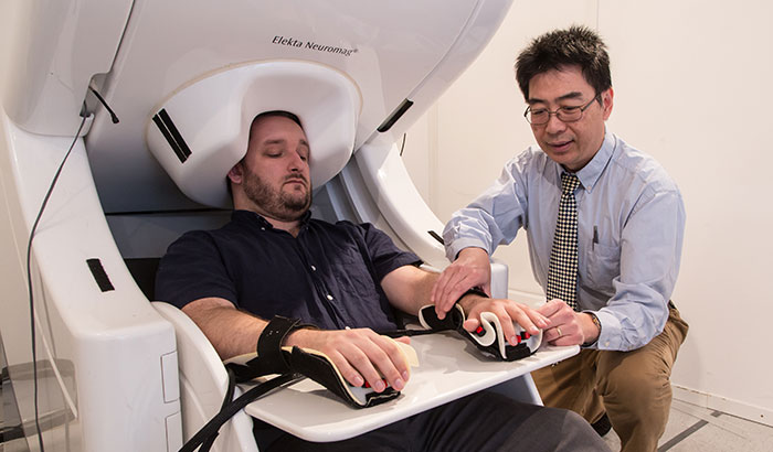 Dr. Mingxiong Huang prepares to do a MEG brain scan on a “healthy control” who has participated in his neuroimaging research. (Photo by Kevin Walsh) 