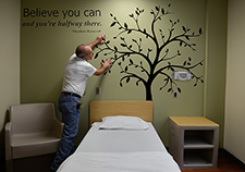 Tony Wickliffe, with the Media Resources group at the Central Arkansas Veterans Healthcare System, applies a mural in a room on an inpatient psychiatric unit. In accord with VA's Mental Health Environment of Care Checklist, the Little Rock facility uses such artwork to avoid conventional picture frames, which could potentially be a hazard. 