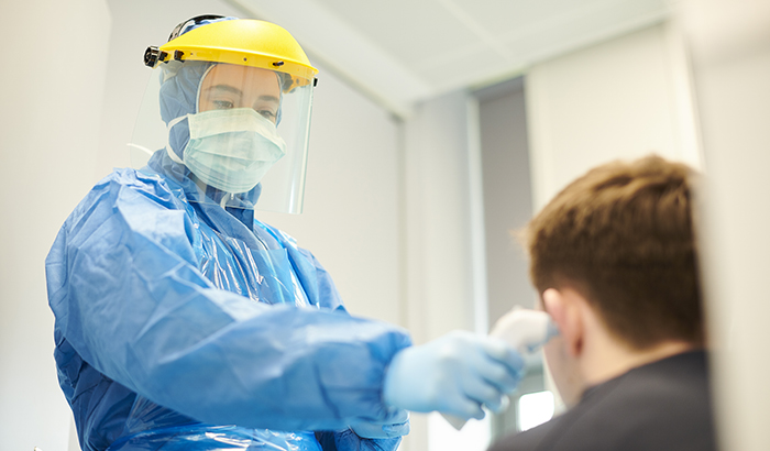 Photo of health care worker in full protective gear taking a patients temperature
