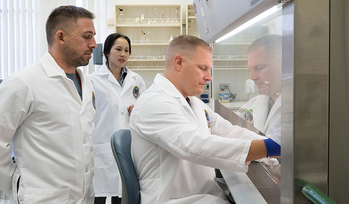 Nick Mezak (left) and Dr. Ngan Huang look on as Nick McMenomy tends to a cell culture inside a biosafety cabinet. (Photo by Adan Pulido) 