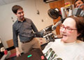 Jan Scheuermann, who has quadriplegia, prepares to take a bite out of a chocolate bar she has guided into her mouth with a thought-controlled robot arm. Research assistants Drs. Brian Wodlinger and Elke Brown watch in the background.  