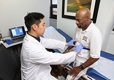 Research technician Michael Tam fits a finger probe on Ralph Liggins, part of a system that will monitor his sleep at his home. (Photo by Jerry Daliege)   